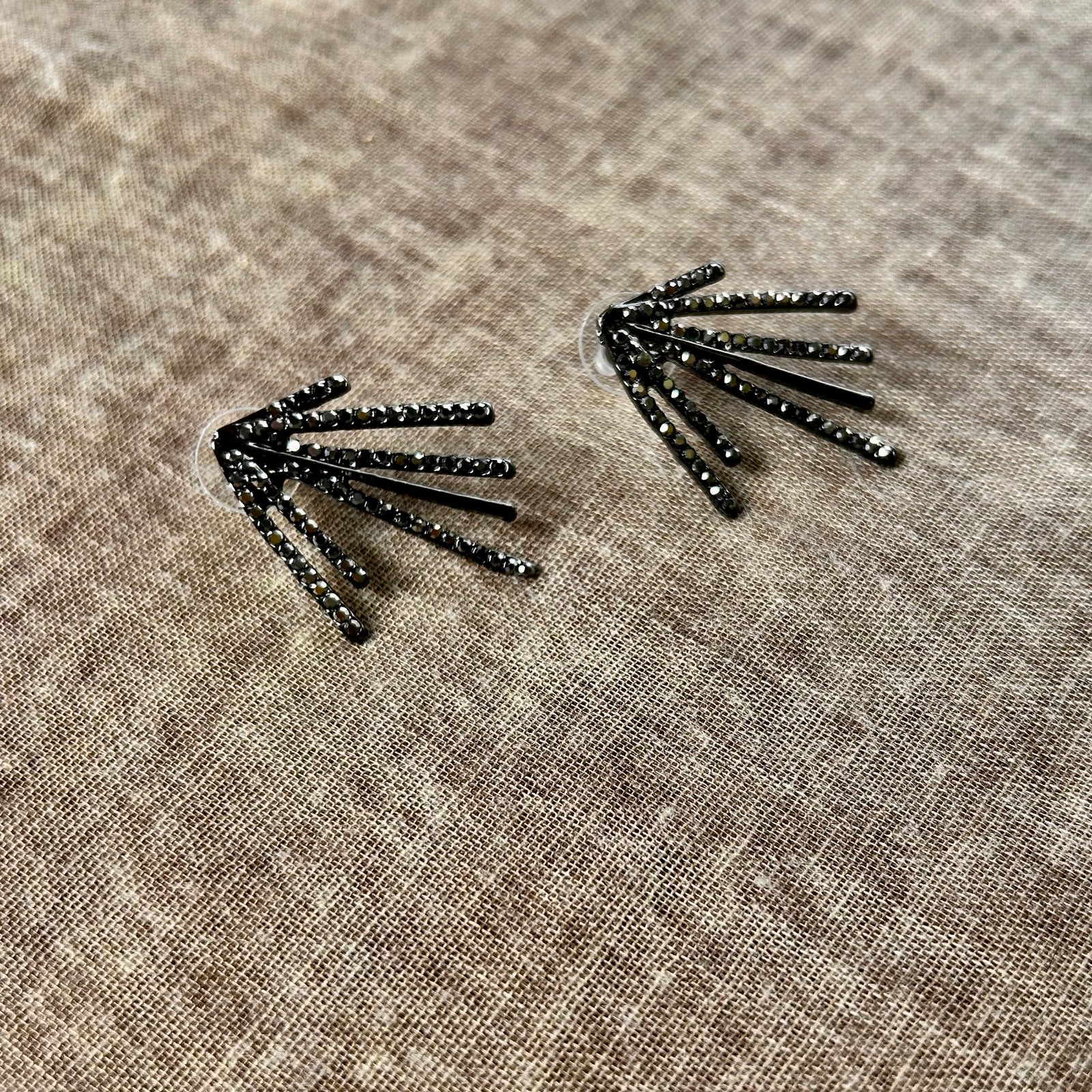Pair of black feather-shaped earrings on a beige fabric background