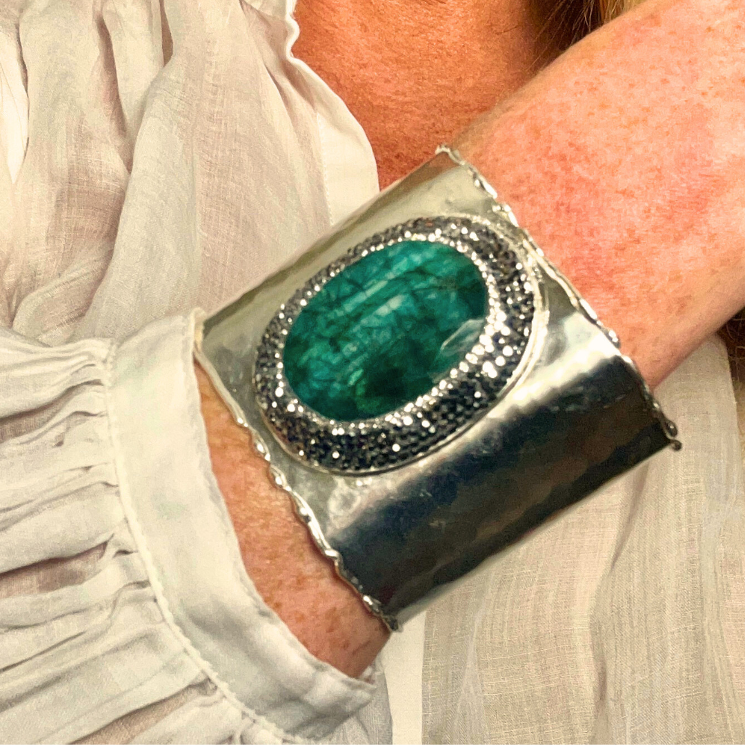 Silver cuff bracelet with a green gemstone worn by a person.