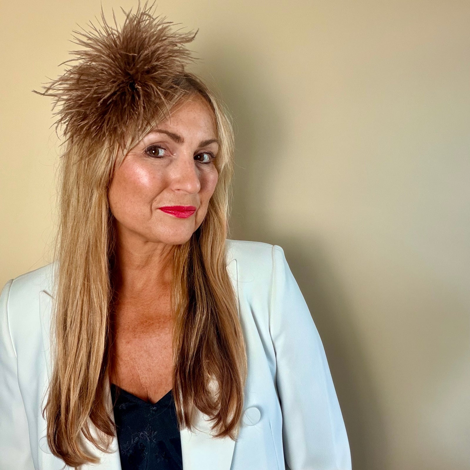 Mannequin wearing a beige blazer with a large brown feathered accessory on a plain background