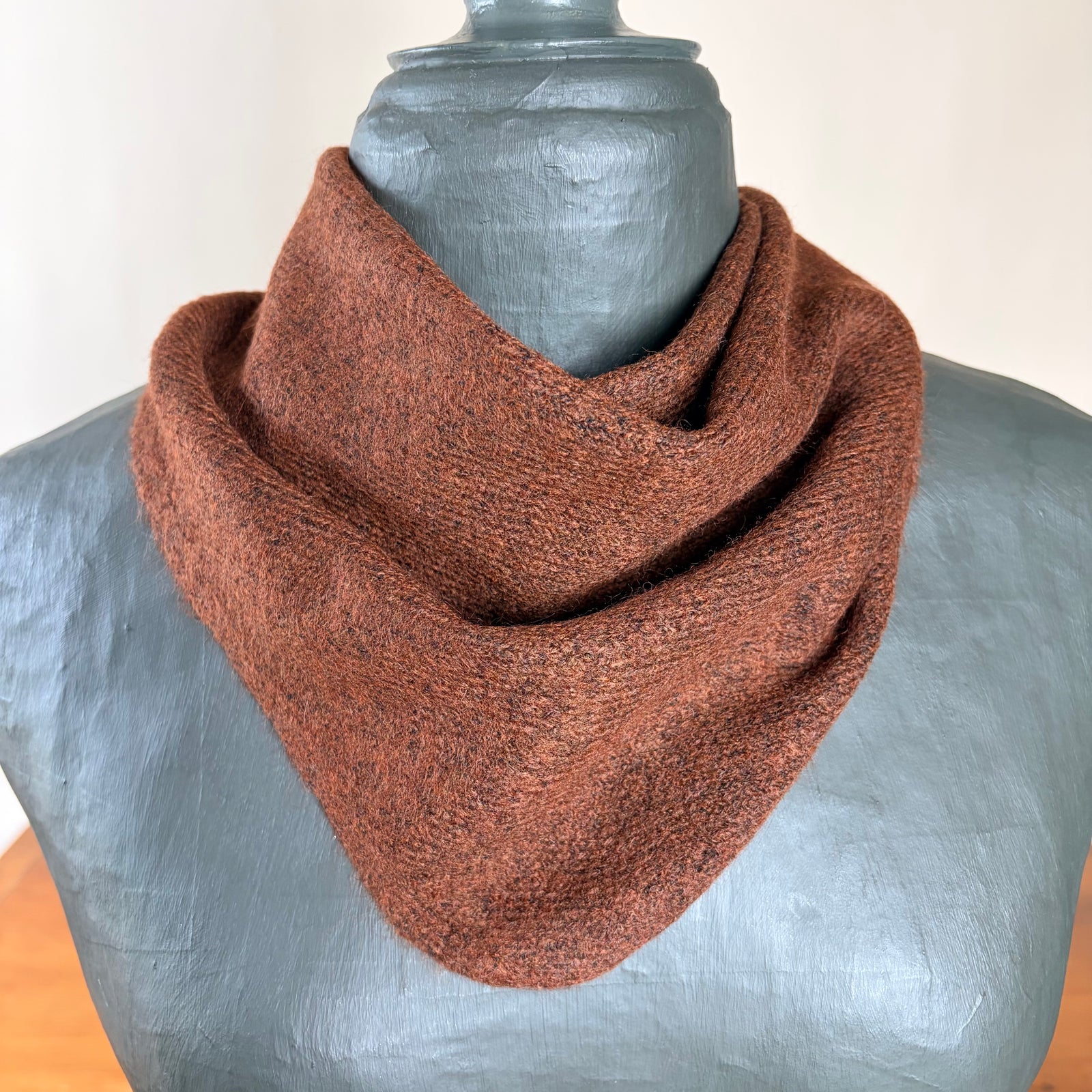 A brown textured knit scarf tied in a knot and draped around a gray mannequin torso, set against a neutral indoor background.