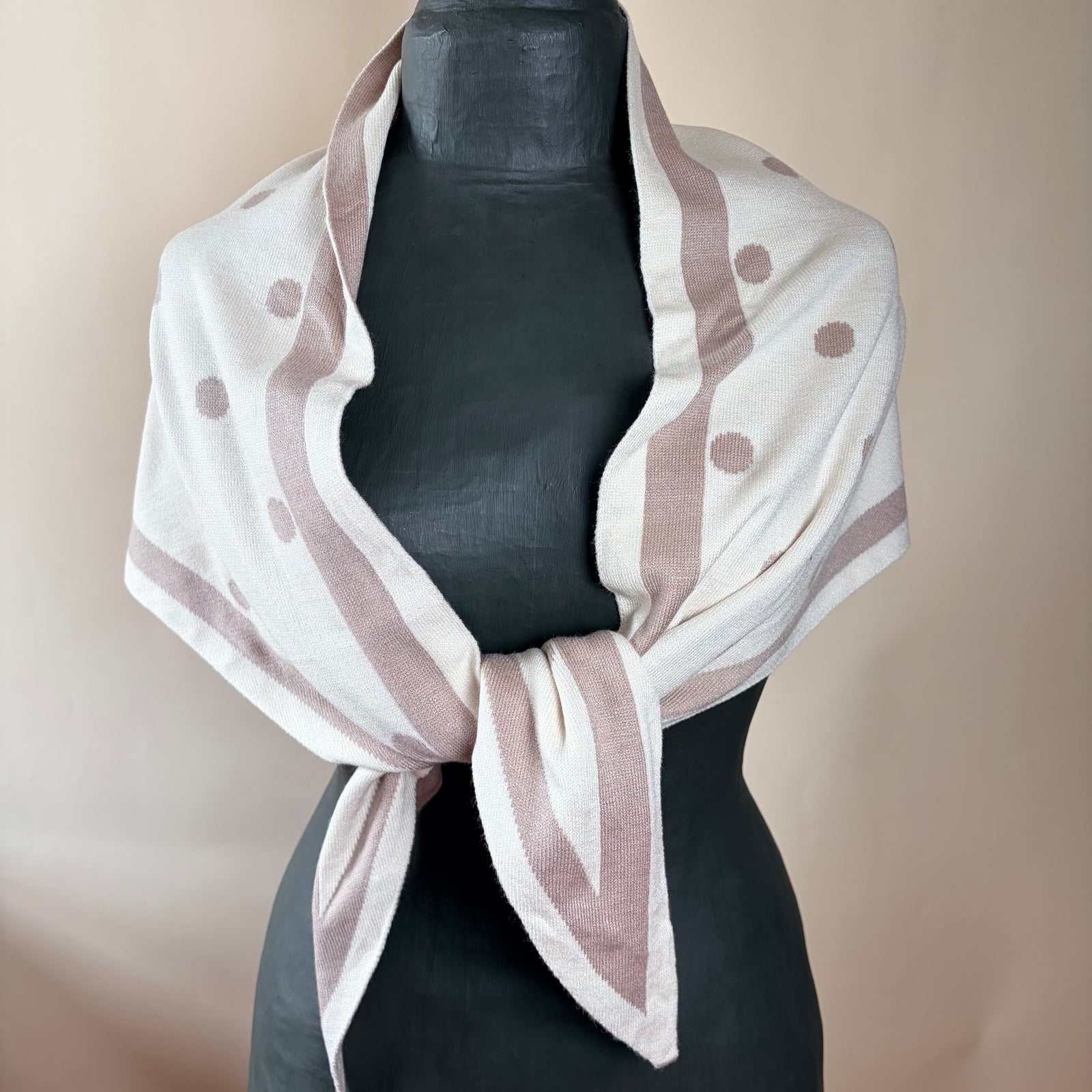 A dusty pink and cream striped scarf with white polka dots, styled on a black mannequin torso against a neutral beige background.