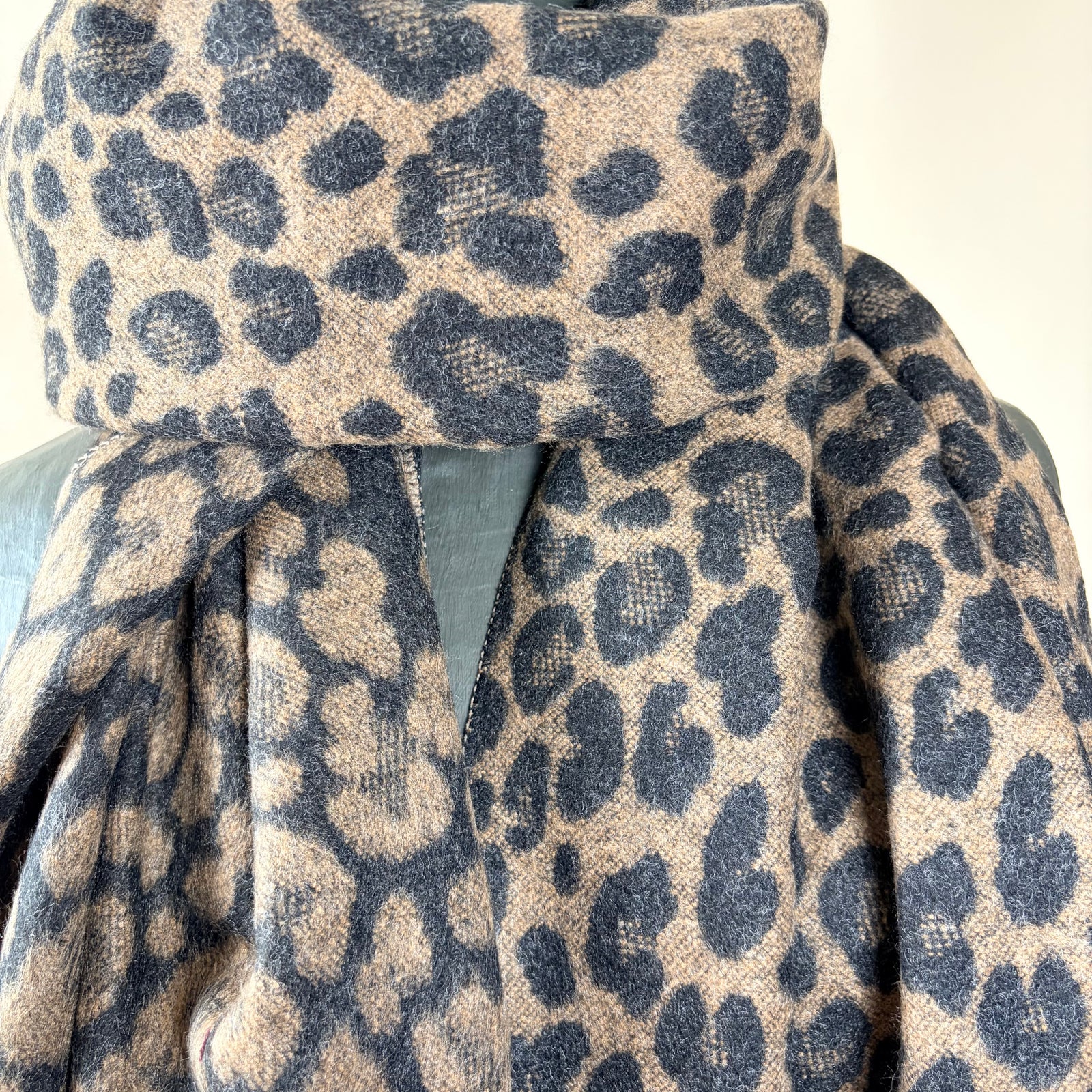 A leopard print scarf in beige and dark navy blue, draped on a dark gray mannequin torso against a plain light beige background.