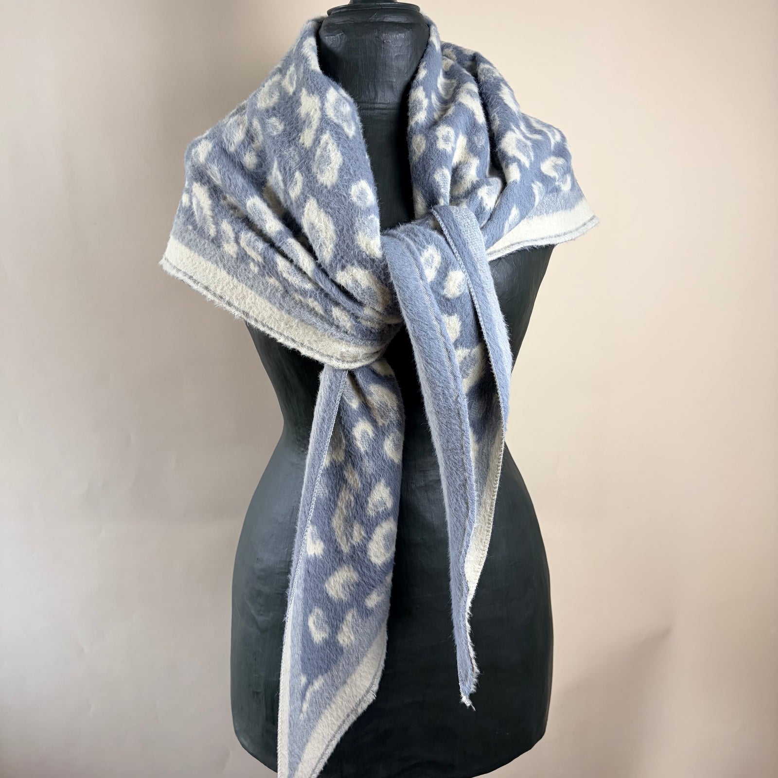 A fuzzy knit scarf with a gray and off-white leopard print pattern, styled on a black mannequin torso against a plain beige background.