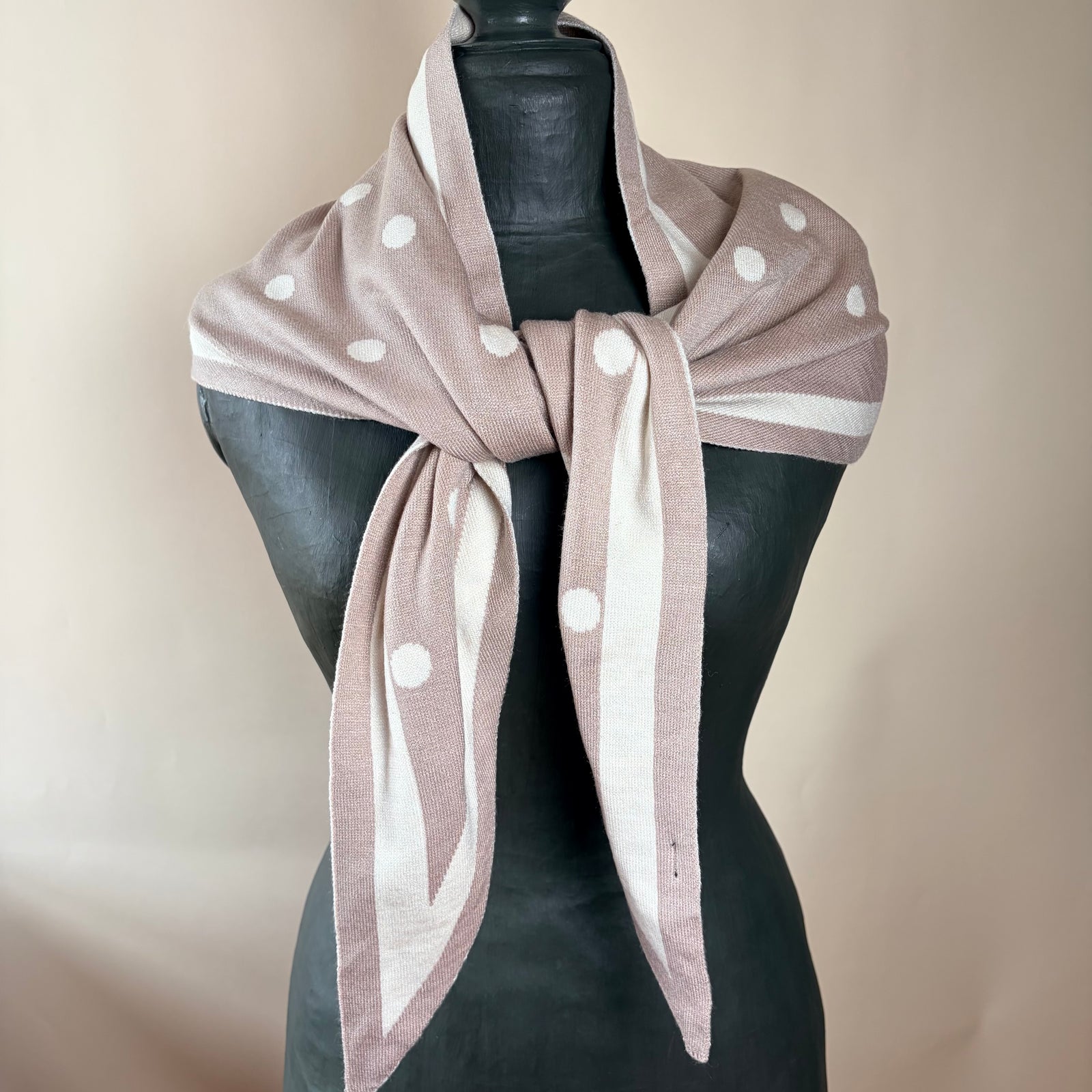 A dusty pink and cream striped scarf with white polka dots, styled on a black mannequin torso against a neutral beige background.