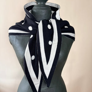 A black and white knit scarf with white polka dots and striped trim, styled on a dark gray mannequin torso against a light beige background.