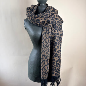 A leopard print scarf in beige and dark navy blue, draped on a dark gray mannequin torso against a plain light beige background.