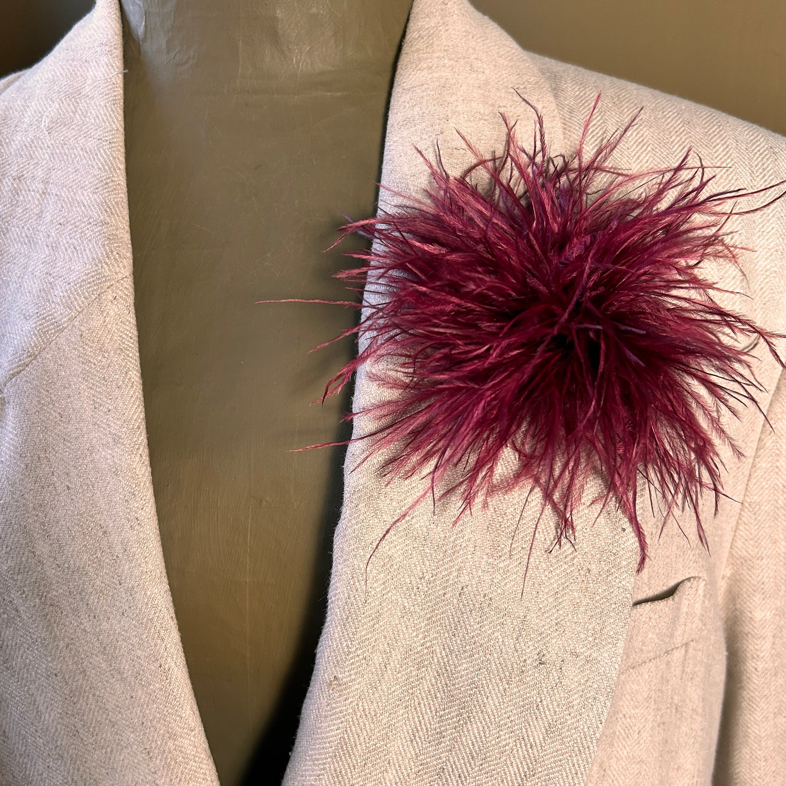 A medium-sized ostrich feather brooch in a deep red color, displayed on a mannequin's jacket.