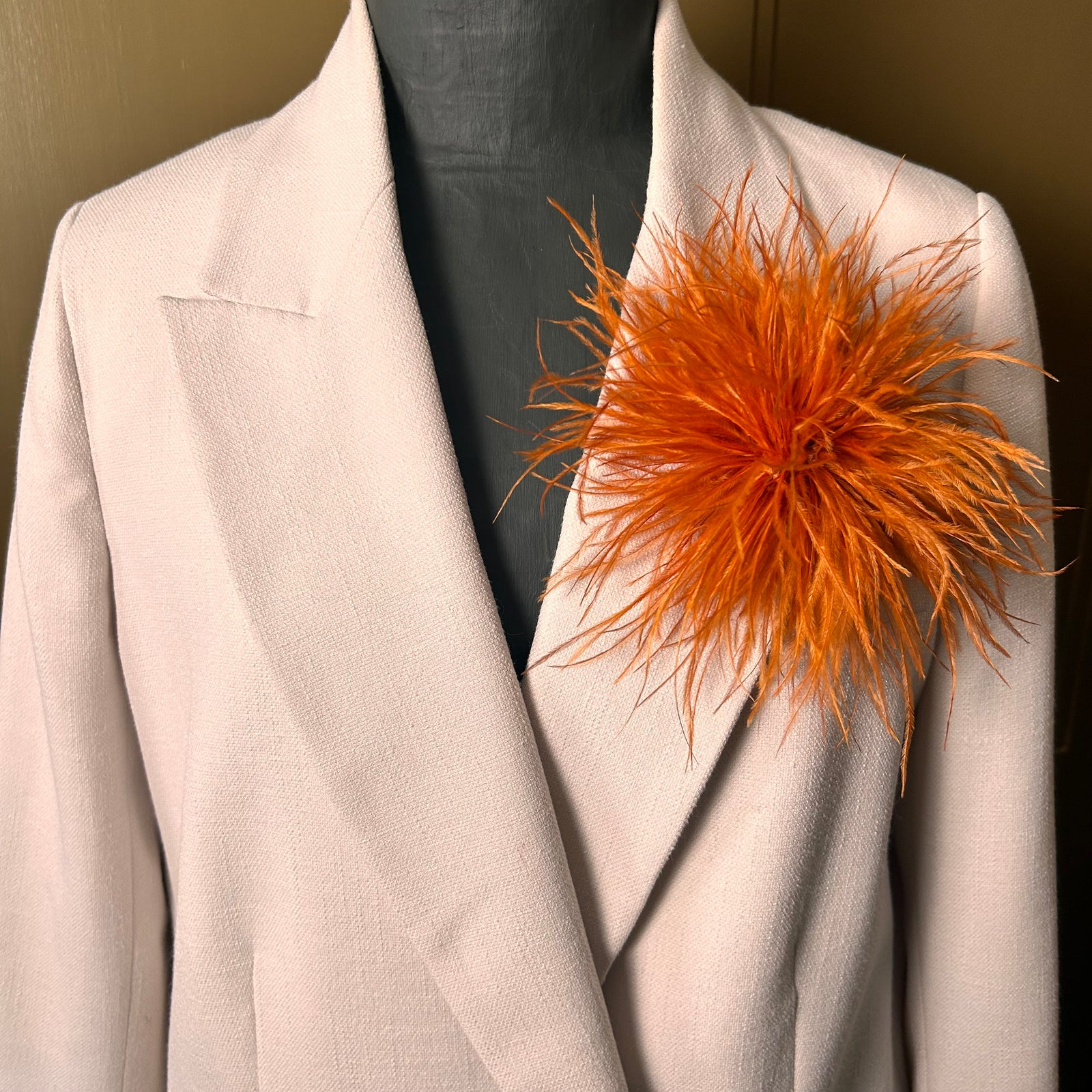 Beige blazer with an orange feathered accessory on a neutral background