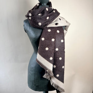 A dark brown and beige woolen scarf with white polka dots and fringed edges, draped on a black mannequin torso against a light beige background.