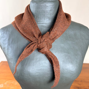 A brown textured knit scarf tied in a knot and draped around a gray mannequin torso, set against a neutral indoor background.