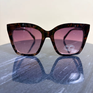 Sunglasses with tortoiseshell frame and pink lenses on a reflective surface.
