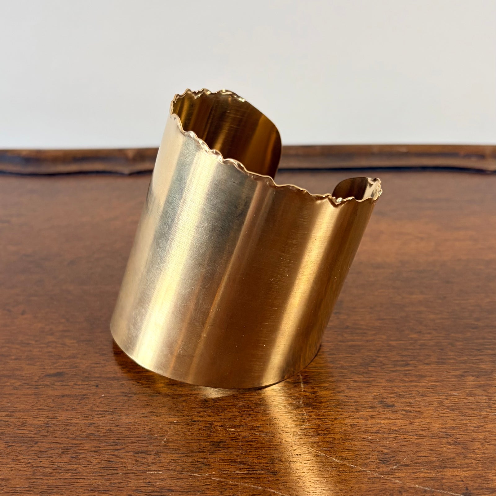 Gold cuff bracelet on a wooden surface with a white background