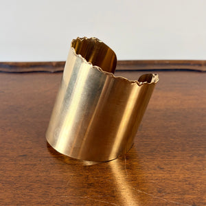 Gold cuff bracelet on a wooden surface with a white background