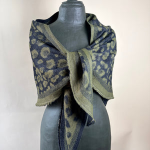 A dark blue and olive green patterned shawl with a textured, fuzzy knit, wrapped around a gray mannequin torso against a plain beige background.