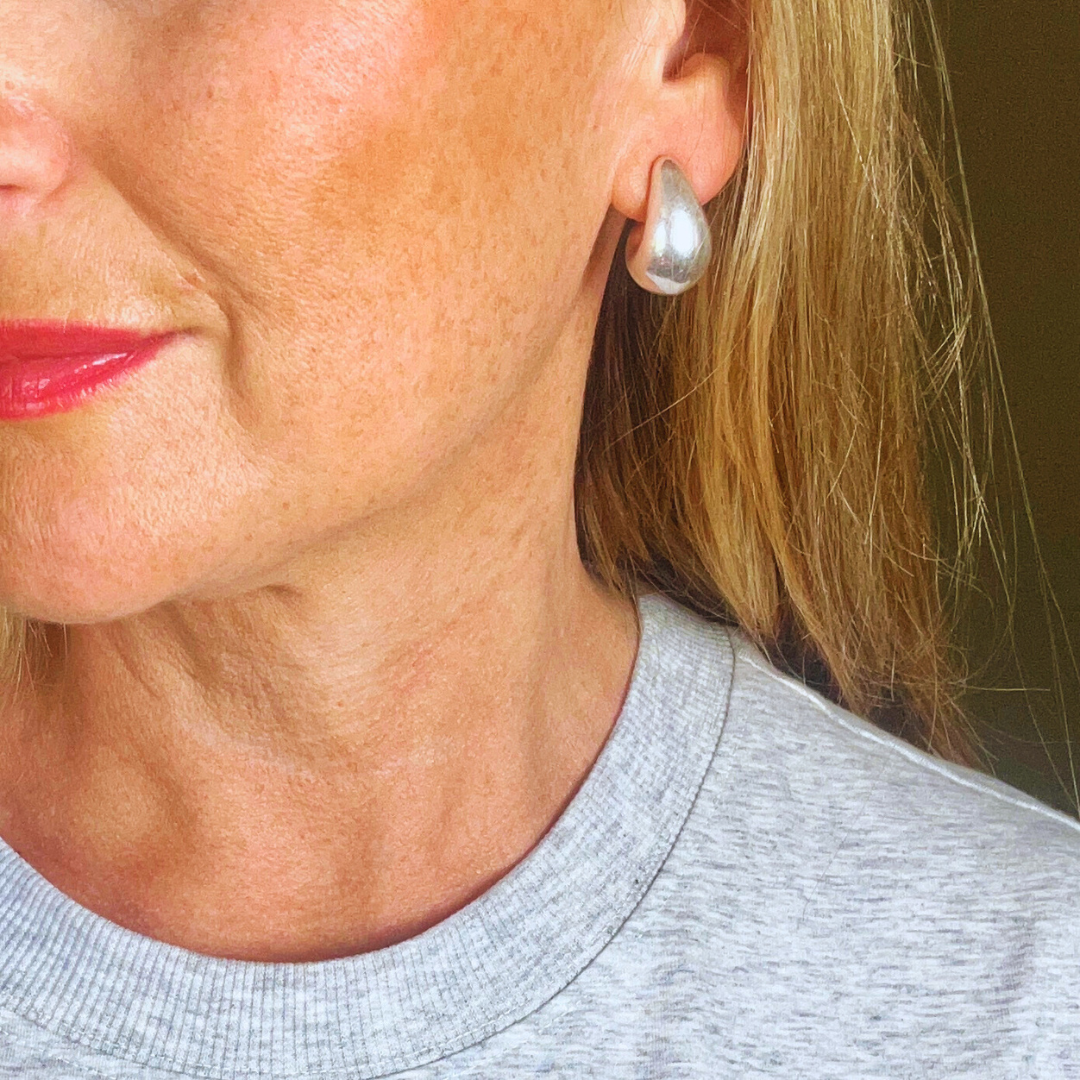 A close-up image of a woman's ear wearing a silver teardrop stud earring.