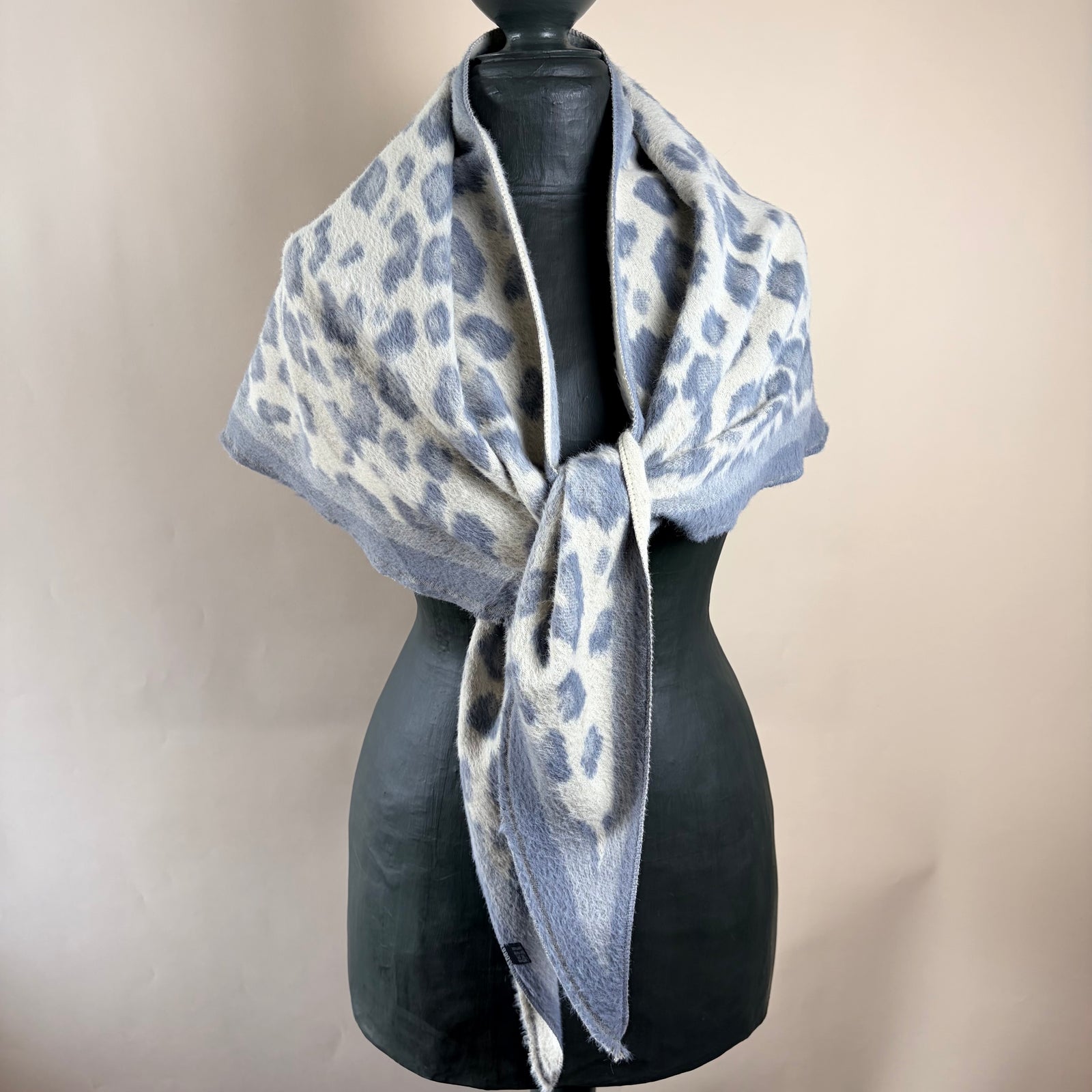 A fuzzy knit scarf with a gray and off-white leopard print pattern, styled on a black mannequin torso against a plain beige background.
