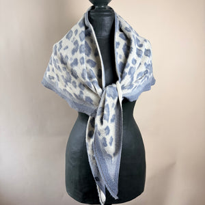 A fuzzy knit scarf with a gray and off-white leopard print pattern, styled on a black mannequin torso against a plain beige background.